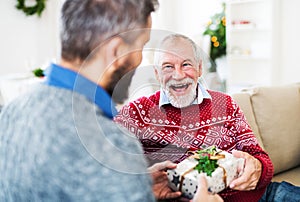 A senior father and adult son with a present sitting on a sofa at Christmas time.