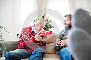 A senior father and adult son with a present sitting on a sofa at Christmas time.