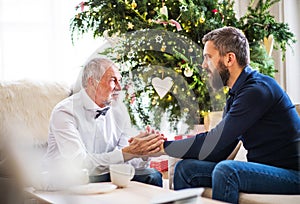 A senior father and adult son sitting on a sofa at Christmas time, looking at each other.