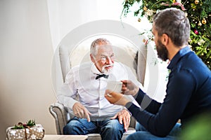 A senior father and adult son sitting on a sofa at Christmas time, talking.