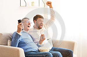 Senior Father And Mature Son Watching Match Celebrating Victory Indoor