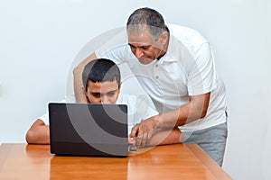 Senior Father and teenage son using laptop. Boy and dad sitting at home working with tablet computer.