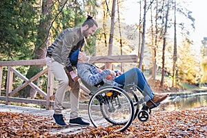 Senior father with wheelchair and his son on walk in nature.