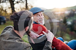 Senior father with wheelchair and his son on walk in nature, talking.