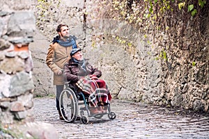 Senior father in wheelchair and son on a walk in old town.