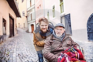 Senior father in wheelchair and young son on a walk.