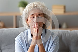 Senior female believer pray at home with hands in prayer