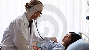 Senior Female doctor checking heart beat of young patient in hospital bed