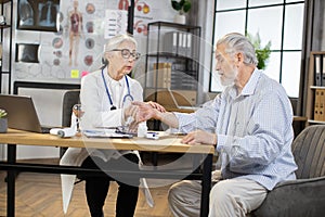 Senior female doctor checking pulse of aged male patient