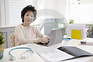 Senior Female Doctor Working At Laptop In Office