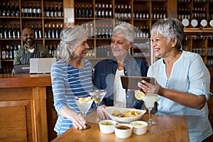 Senior female friends using digital tablet while having drinks