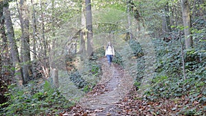 Senior female hiker walking on wooden path in a between trees and wild vegetation