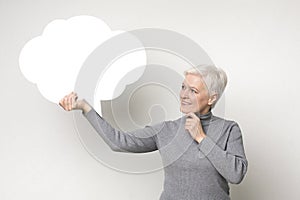 Senior female holding blank speech bubble on light studio background