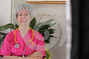 Senior female nurse wearing pink scrubs and yellow stethoscope