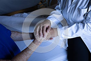 Senior female patient holding hands of doctor in hospital room