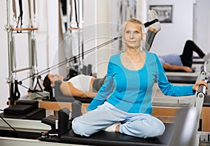 Senior female performing mermaid exercise on reformer Pilates machine for improving and maintaining mobility in gym