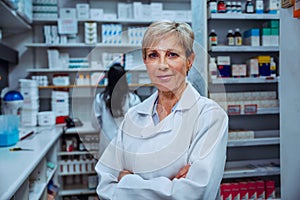 Senior female pharmacist standing with cross arms in pharmacy drug store