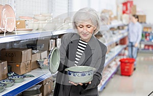 Senior female shopper choosing soup tureen at Asian store