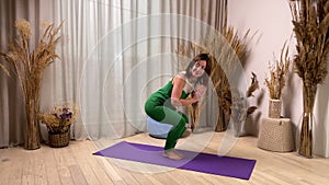 Senior female in sport suit exercising, performing chair pose indoors