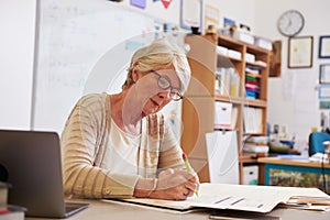 Senior female teacher at her desk marking studentsï¿½ work