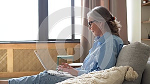 Senior female typing email on laptop, blogging, writing message, working on project from home