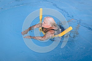 Senior female woman holds on to a flotation device on a swimming pool to learn how to swim