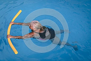 Senior female woman holds on to a flotation device on a swimming pool to learn how to swim