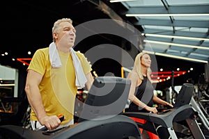 Senior fitness enthusiasts engaged in treadmill session at modern fitness center. Active older couple staying fit with