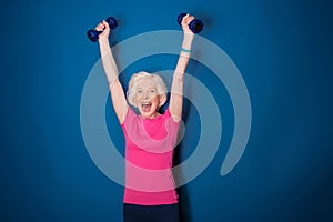 Senior fitness woman training with dumbbells isolated on blue