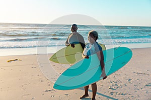 Senior frican american couple with surfboards standing at sandy beach against sea and sky