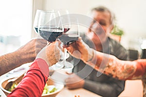 Senior friends cheering with red wine glasses at restaurant lunch - Happy mature people having fun drinking and eating together -