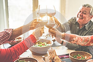 Senior friends cheering with wine glasses at home lunch - Happy mature people having fun together - Focus on left bottom glass -