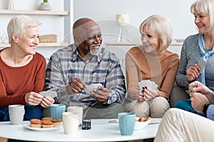 Senior friends playing cards while drinking tea at home