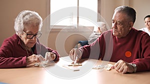 Senior friends playing dominoes at table in nursing home