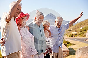 Senior Friends Visiting Tourist Landmark On Group Vacation With Arms Raised