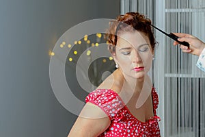 Senior glamour woman in red and black dress with hairdresser preparing to further hairstyle with comb