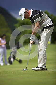 Senior golf player putting at hole.