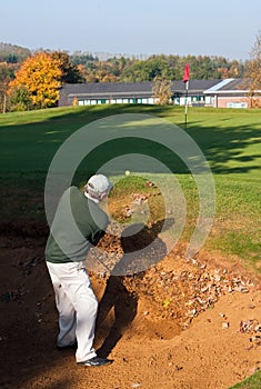 Senior golfer playing out of a bunker in autumn