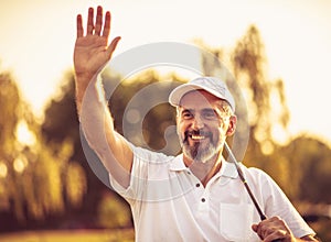 Senior golfer standing on court. Man waving