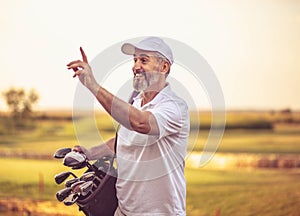 Senior golfer walking on golf court with bag.