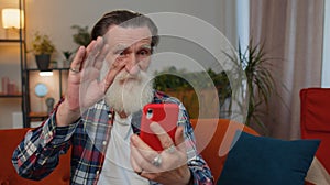 Senior grandfather man making phone conversation call with family sitting on couch at home in room