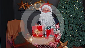 Senior grandfather parodies Santa Claus presenting Christmas gift box, holidays celebration at home