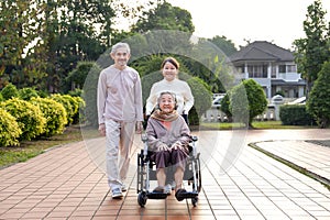 senior grandma sitting on wheelchair,smiling,daughter and son in law walking with her in the city park
