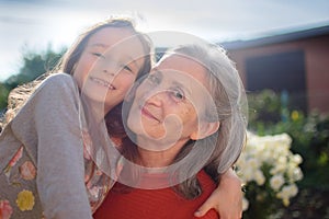 Senior grandmother with gray hair wearing red sweater with her little granddaughter are hugging in the garden and during