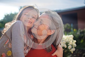 Senior grandmother with gray hair wearing red sweater with her little granddaughter are hugging in the garden and during