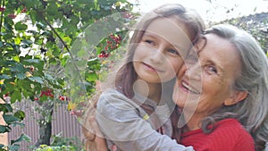 Senior grandmother with gray hair wearing red sweater with her little granddaughter are hugging in the garden and during