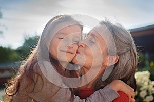 Senior grandmother with gray hair wearing red sweater with her little granddaughter are hugging in the garden and during