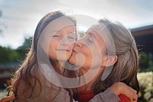 Senior grandmother with gray hair wearing red sweater with her little granddaughter are hugging in the garden and during