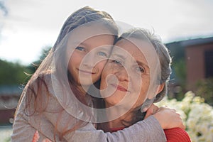 Senior grandmother with gray hair wearing red sweater with her little granddaughter are hugging in the garden and during