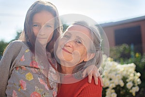 Senior grandmother with gray hair wearing red sweater with her little granddaughter are hugging in the garden and during